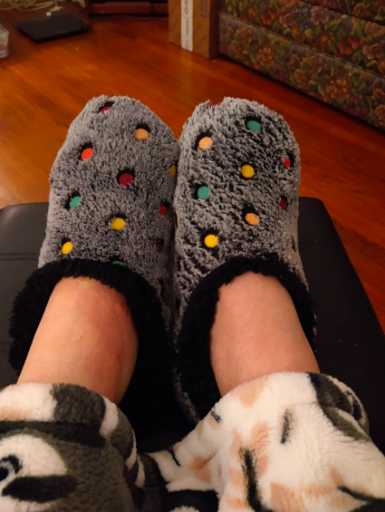 a reviewer wearing the black fuzzy slippers with colorful polka dots