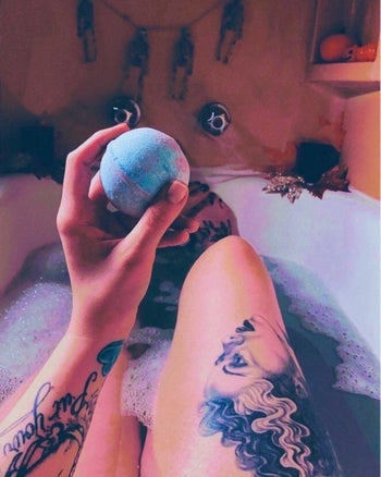 A reviewer holding a bath bomb while relaxing in a colorful bath
