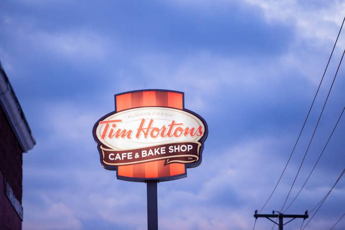 A photo of a Tim Hortons sign against a blue sky with power lines near by.