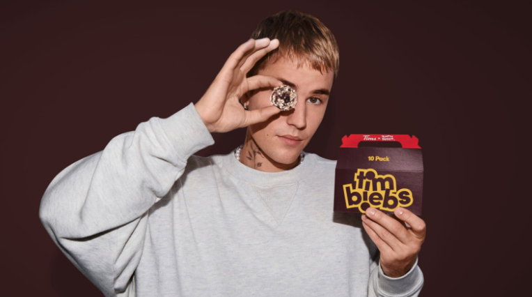 Justin Bieber holding up a Timbiebs to his eye while holding a box of Timbiebs