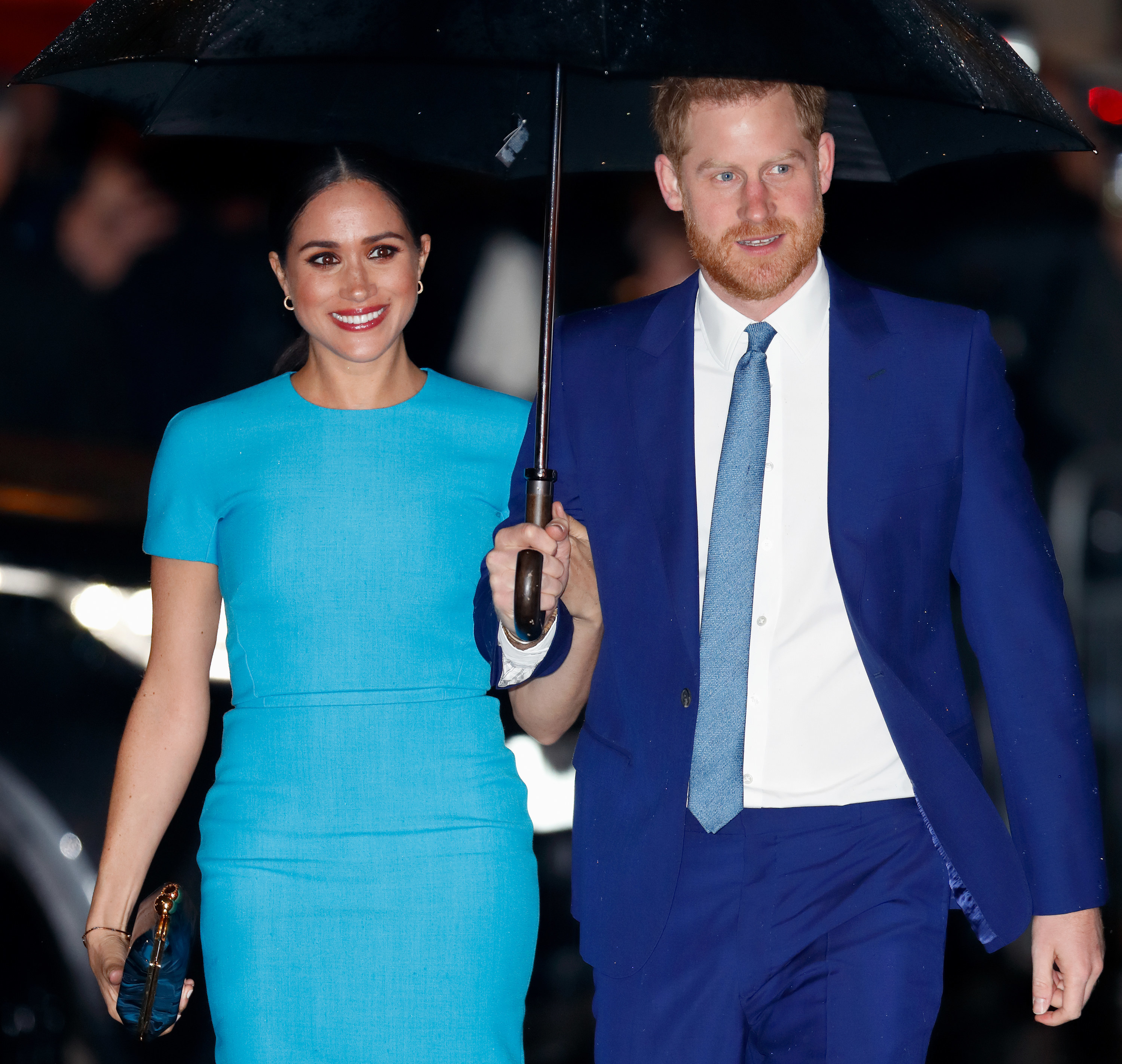 Harry and Meghan walking to an event while holding an umbrella