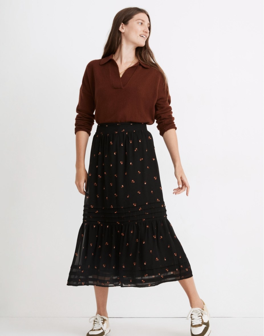 model wearing the black maxi skirt with brown floral detailing and a brown sweater with brown and white sneakers