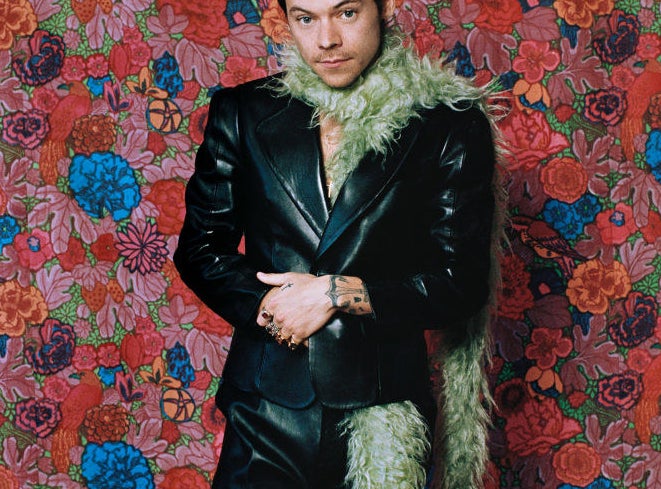 Harry Styles wearing a fluffy green scarf in front of a floral wallpaper