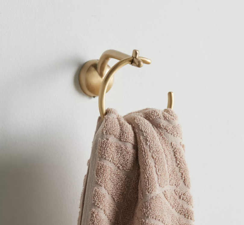 A gold hand towel ring with a towel hanging off of it