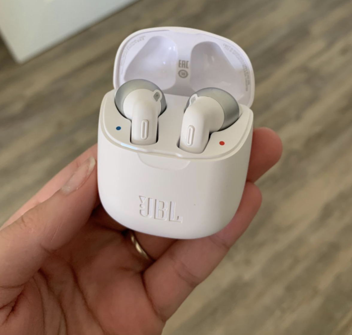 reviewer holding the white jbl headphones in their charging case