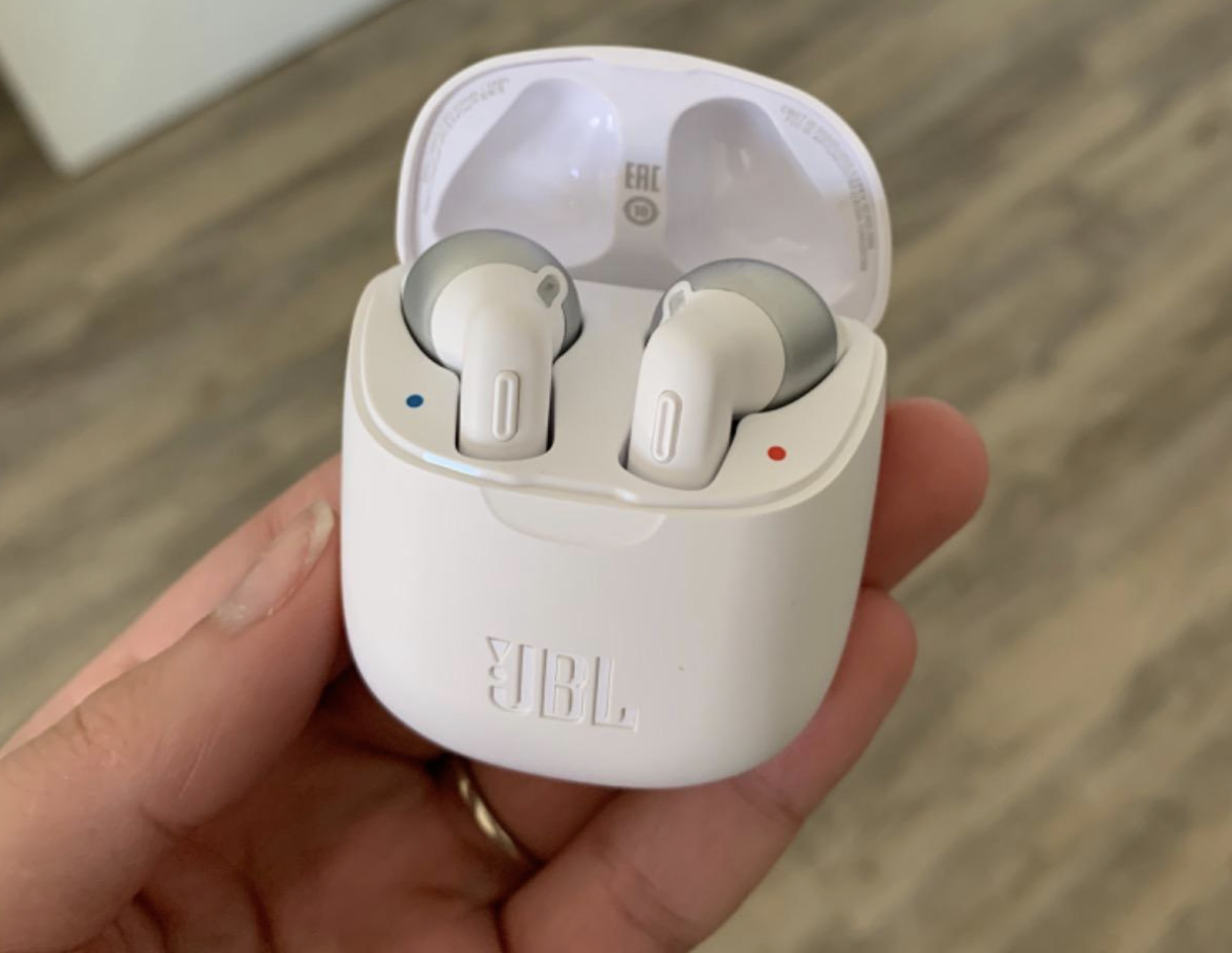 reviewer holding the white jbl headphones in their charging case