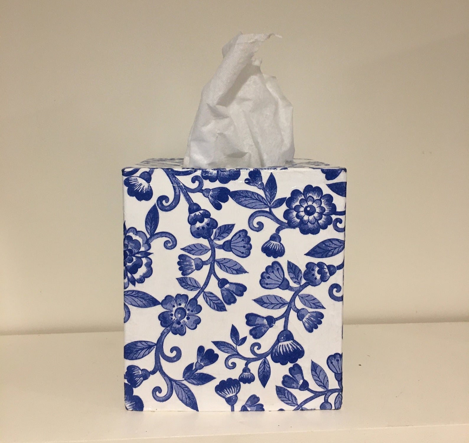 The white tissue box cover with blue flowers and vines painted throughout