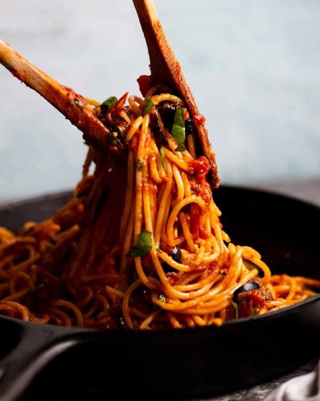 Lifting spaghetti alla puttanesca out of a skillet to serve