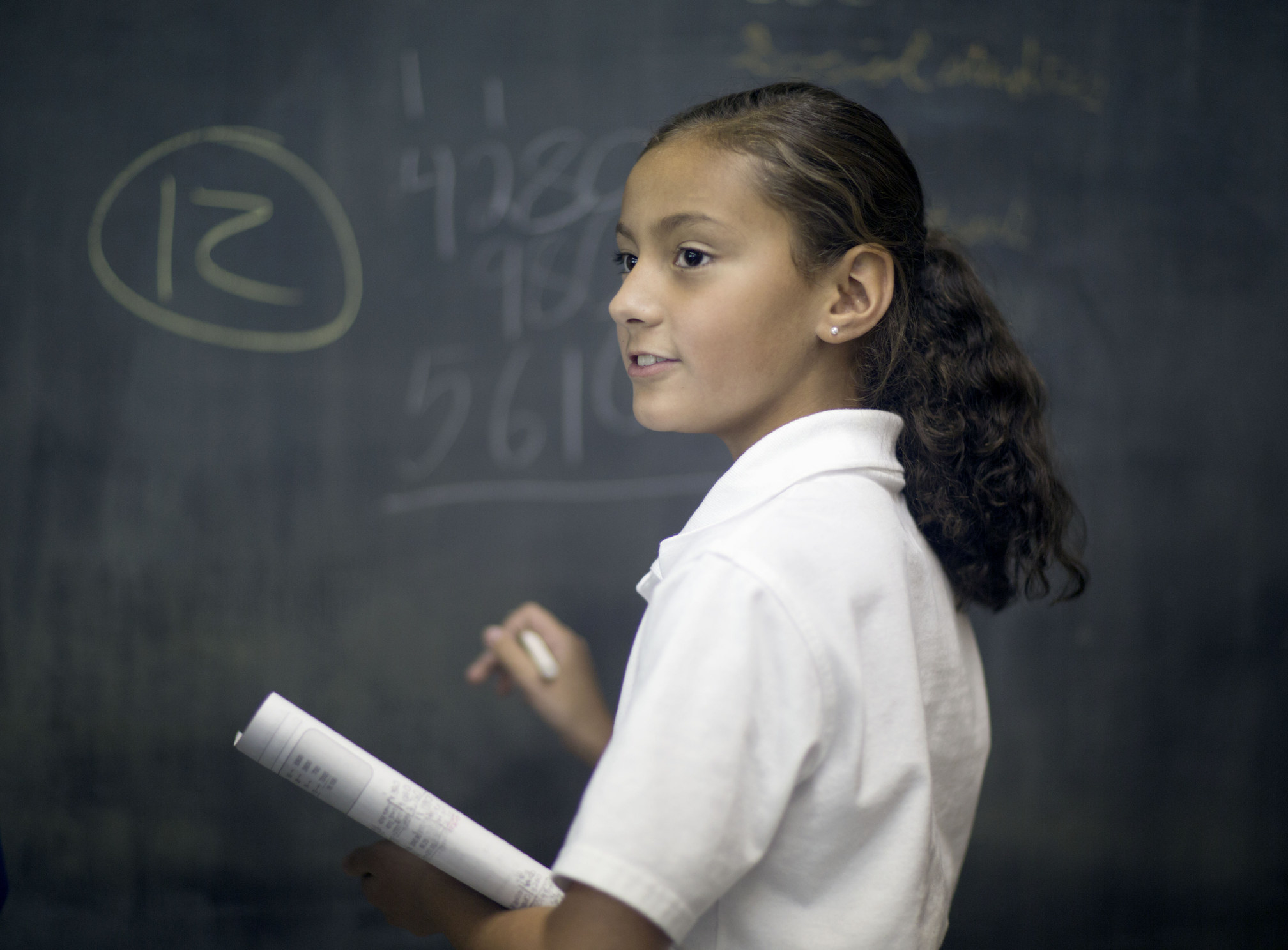 A Latinx student solves a math problem on a chalkboard