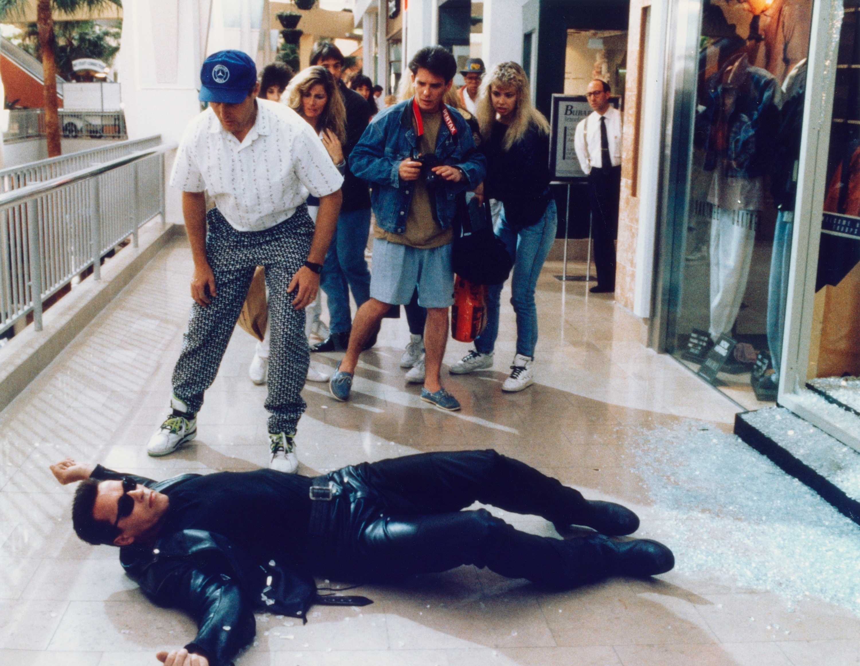 Arnold Schwarzenegger lays on the floor of a mall while shoppers look on