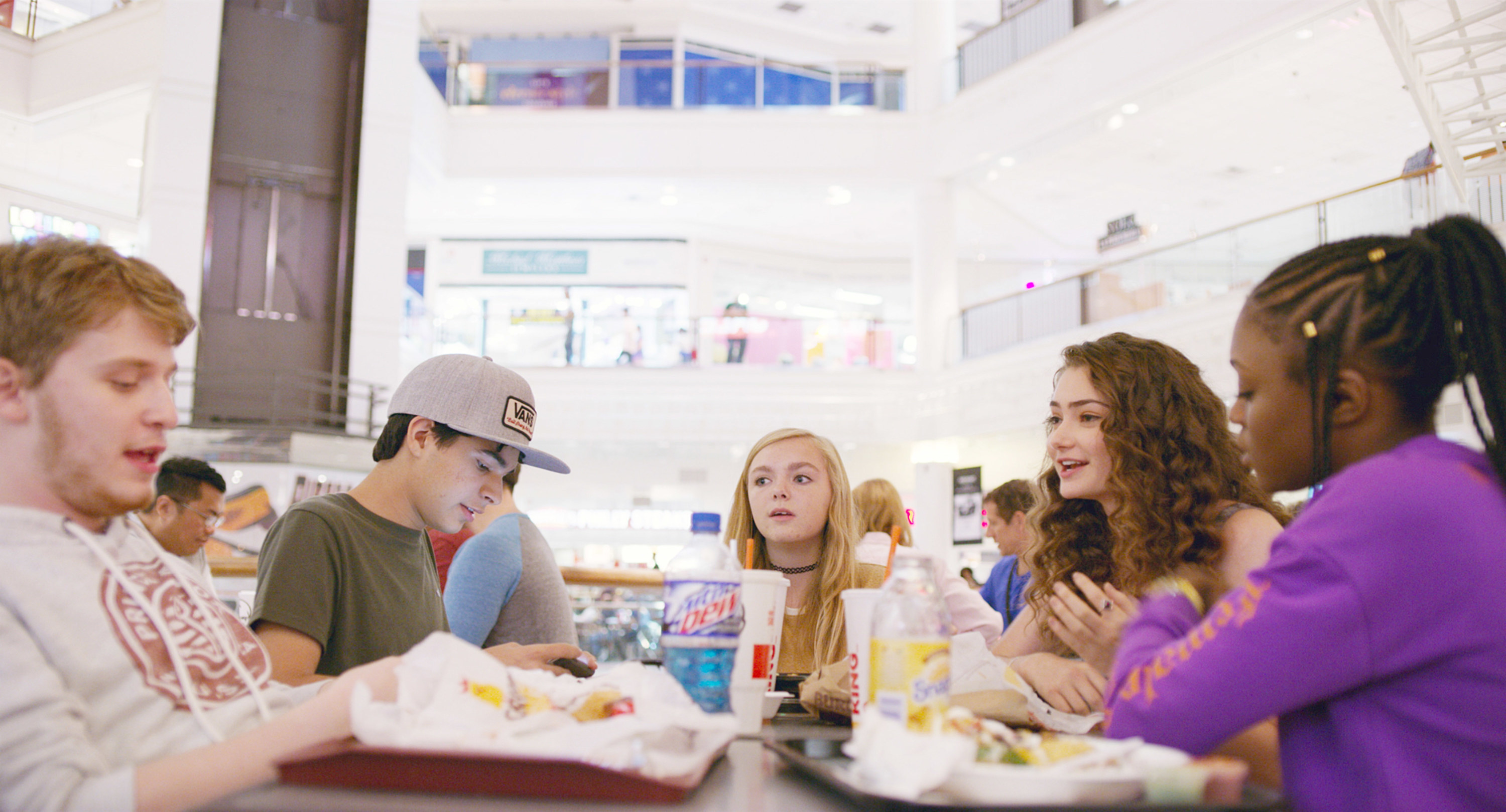 Elsie Fisher sits at a food court table with Fred Hechinger, Daniel Zolghadri, Emily Robinson, and Imani Lewis