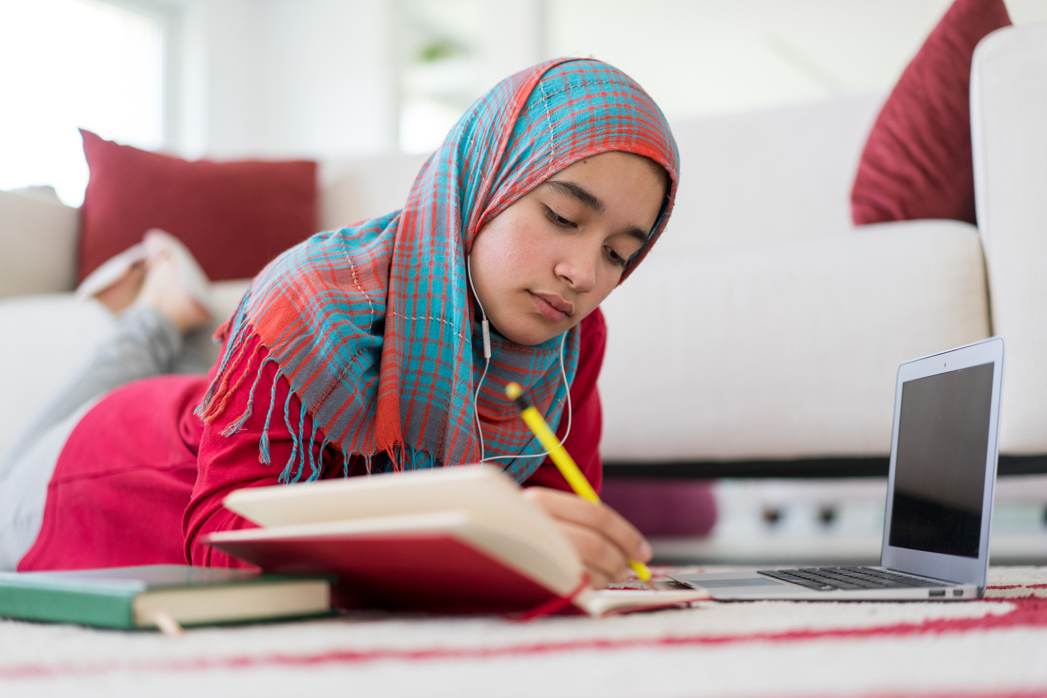 A Middle Eastern teenage girl with hijab studying at home
