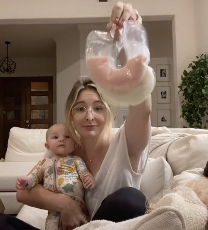 Jo holding her baby in one arm and two bags of her breastmilk, one white in color and the other pink, in the other arm