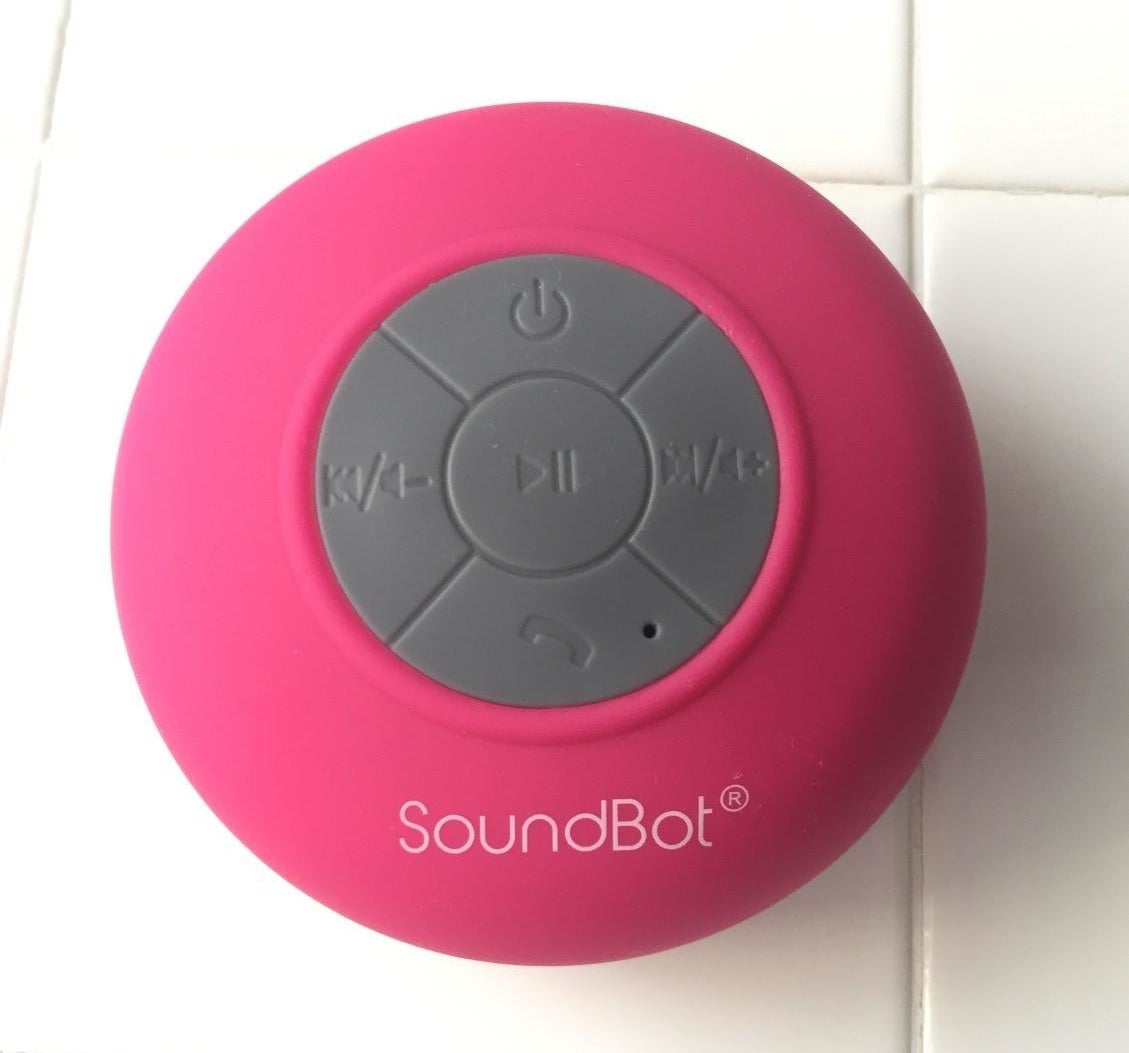 The pink SoundBot suctioned to a white tile shower wall