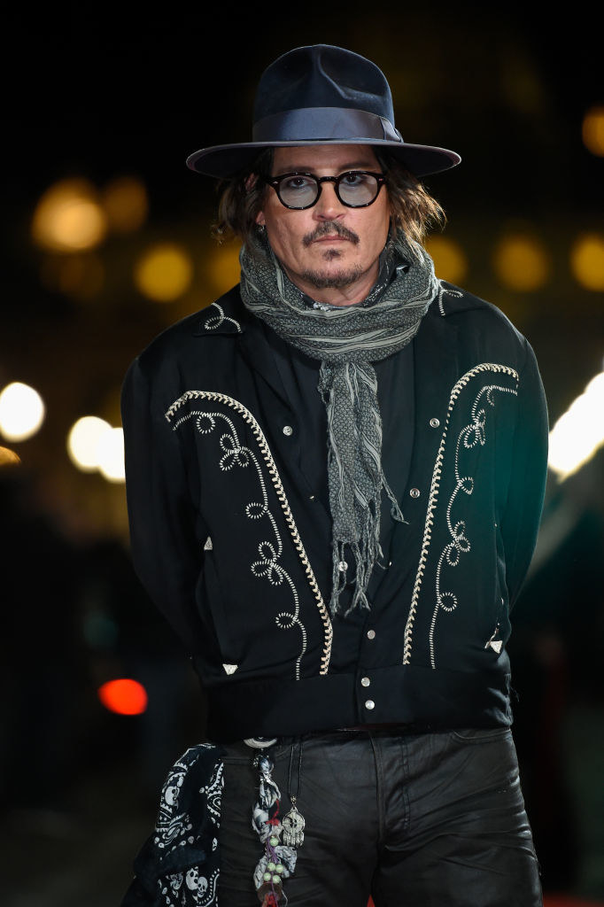 Johnny wearing a fedora, scarf, and embroidered jacket at the puffins premiere