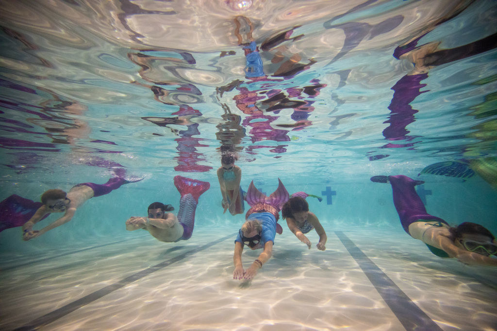 A group of people swim underwater with mermaid tails on