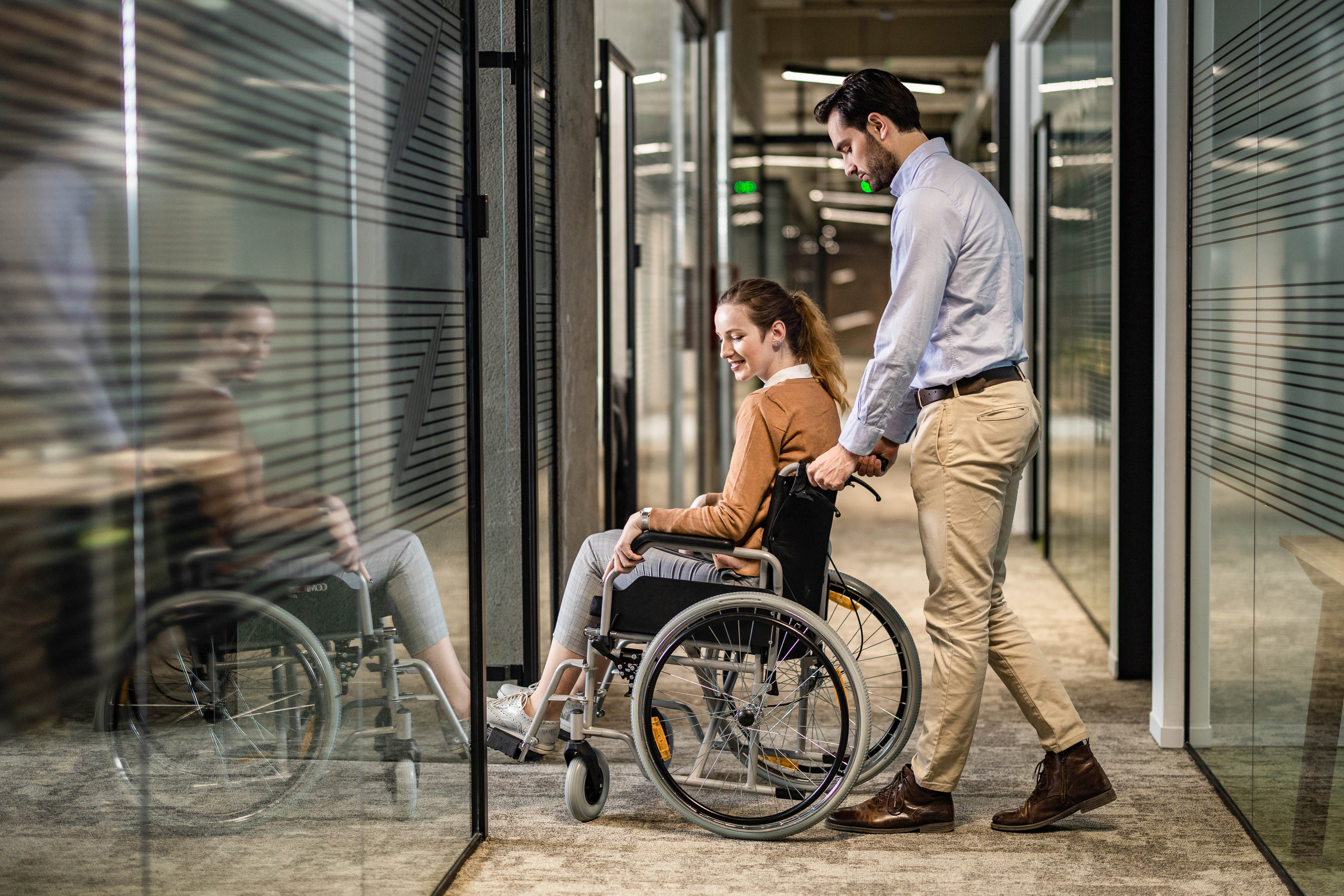 Man pushing a coworker in a wheelchair through a doorway