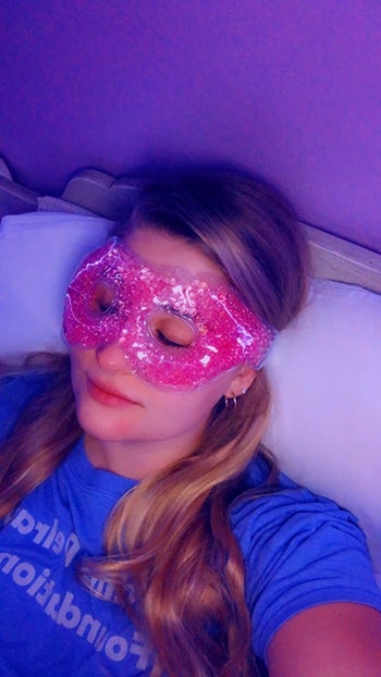 Reviewer laying down with their eyes closed while wearing the pink eye mask