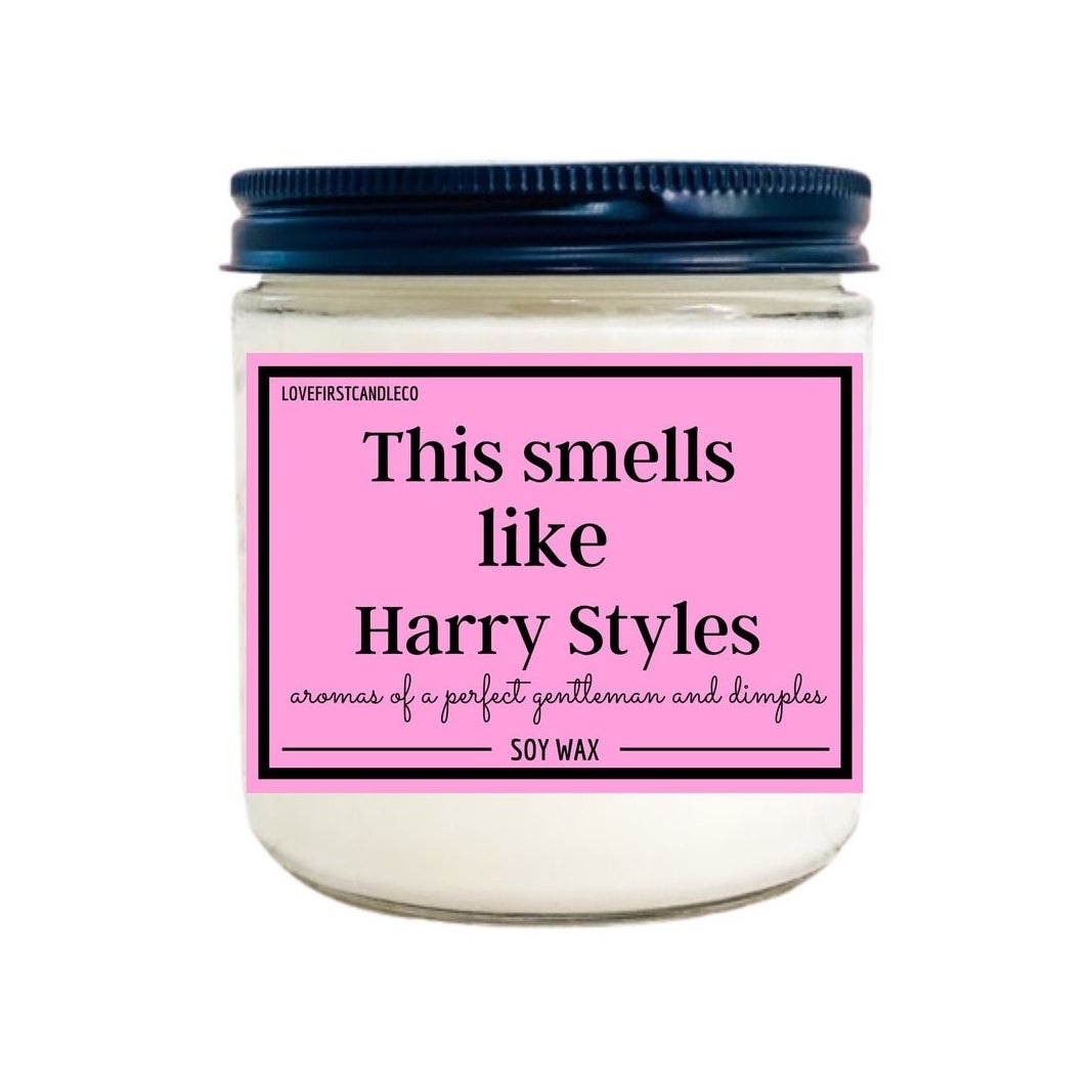 a white soy candle in a jar with a black top and a pink label that reads &quot;This smells like Harry Styles&quot;.