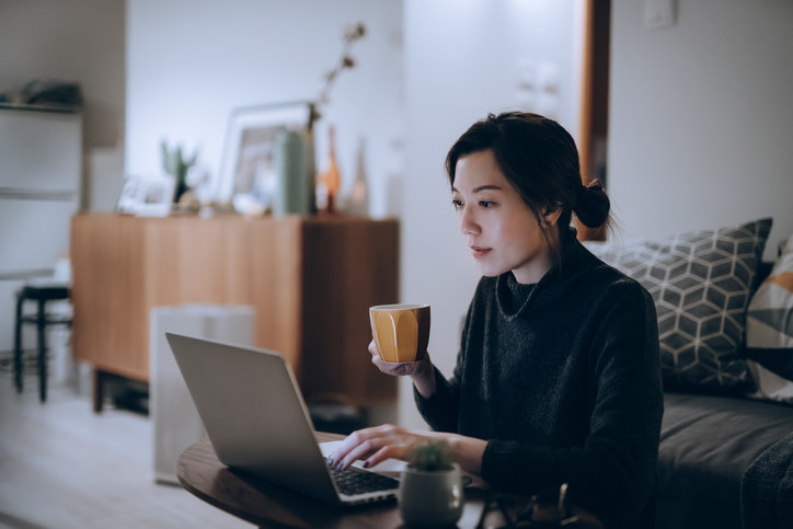 A woman holds a mug and appears focused on her laptop