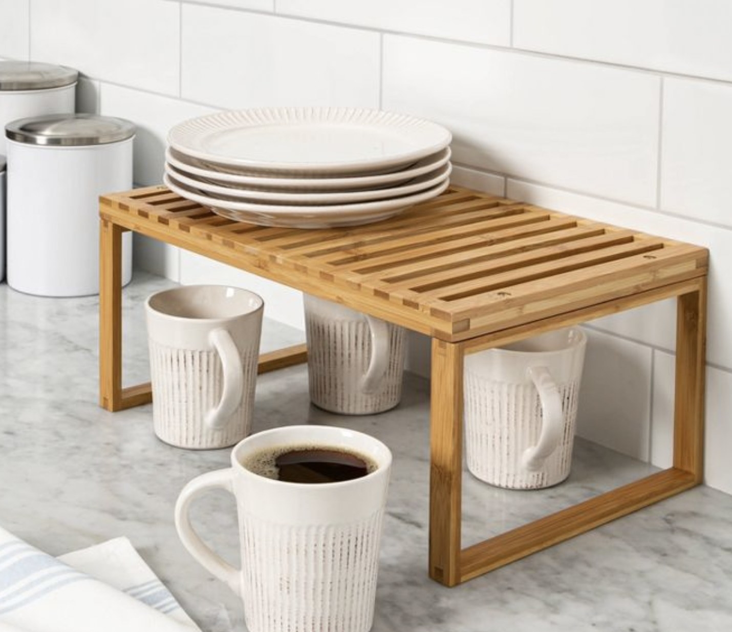 a bamboo shelve in a counter holding plates and hovering over mugs