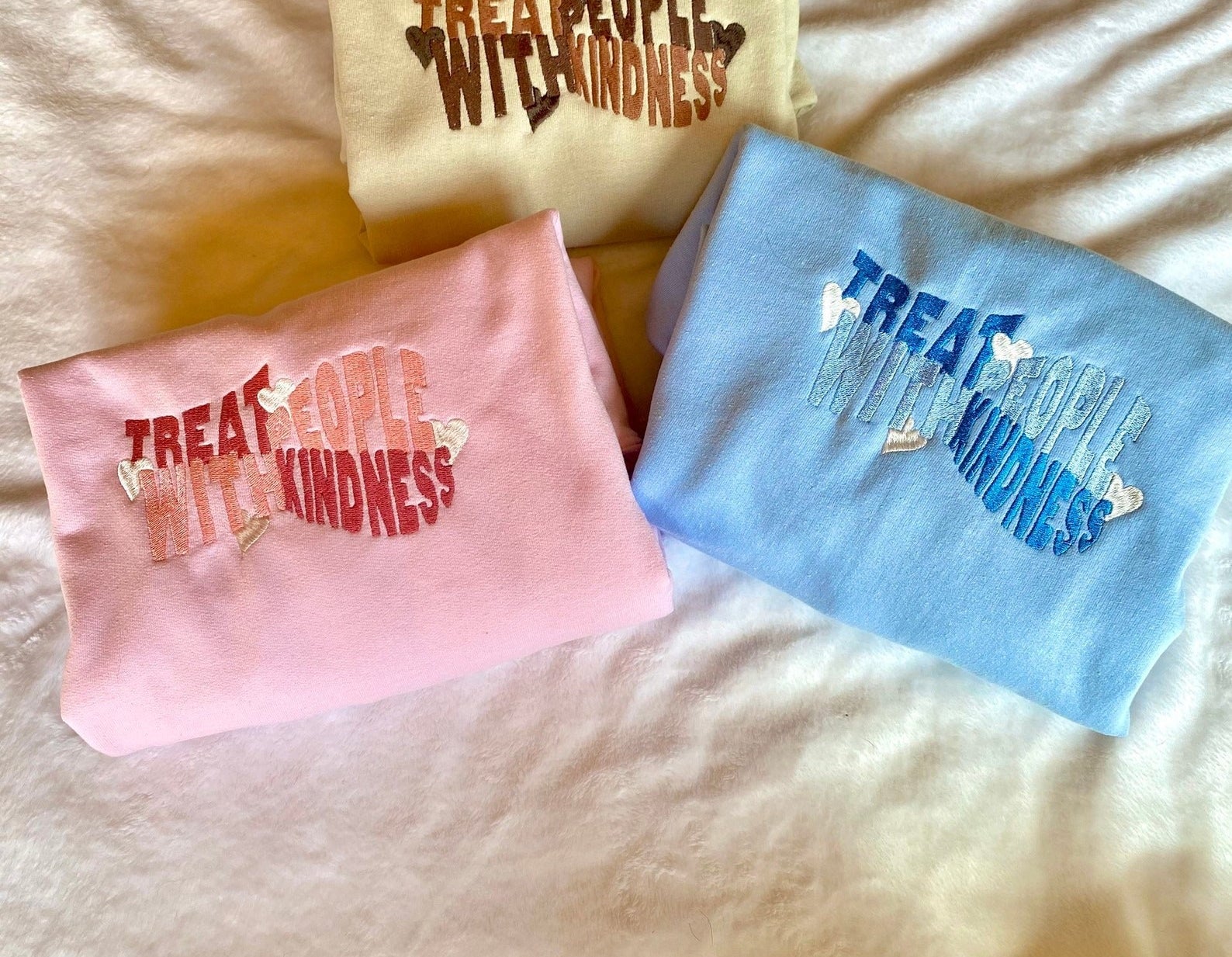 The sweaters embroidered with treat people with kindness in pink, blue, and yellow
