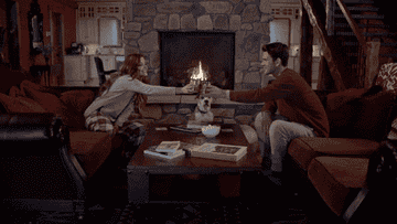 Gif of two people clinking cups in front of a fireplace