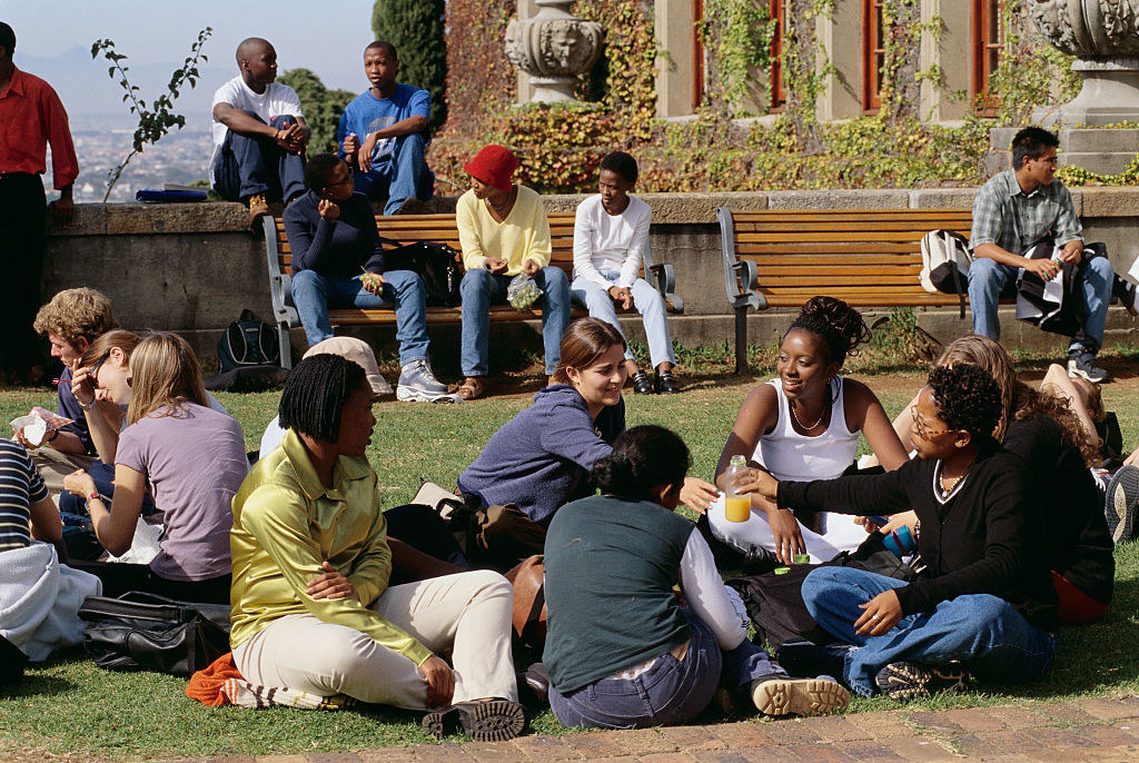 Groups of University of Cape Town students sit outside, chatting in a school plaza