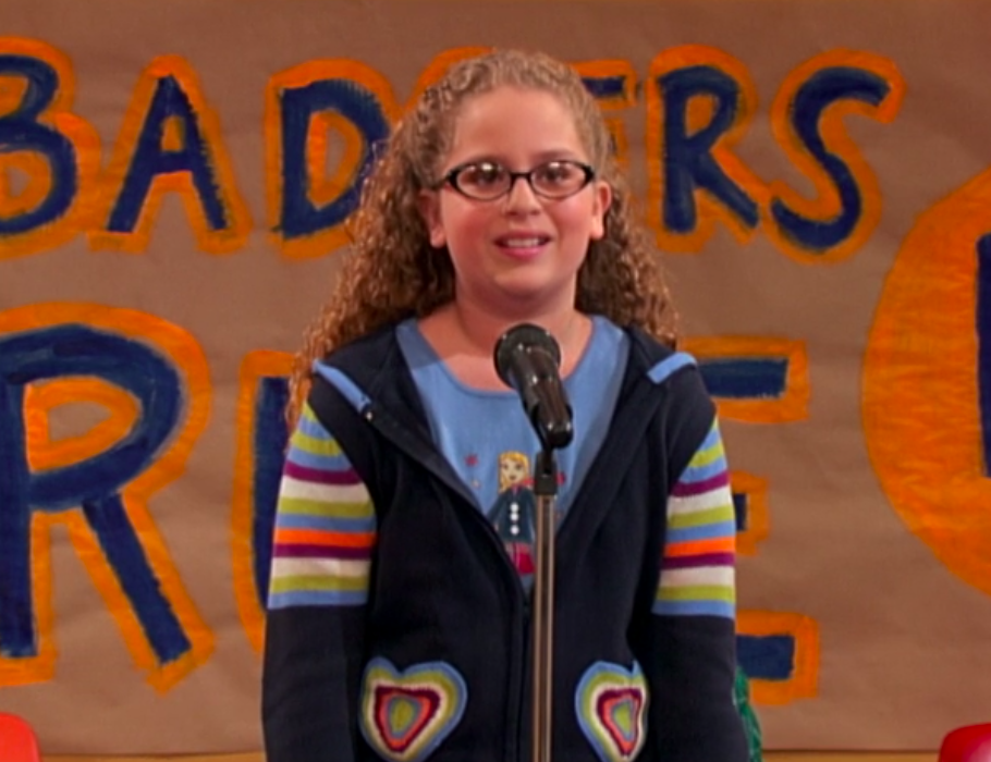 Allie with long, curly hair and chunky glasses filming a scene of &quot;Suite Life&quot;