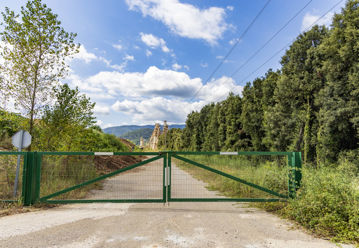 A wide, green gate with a dirt road behind it