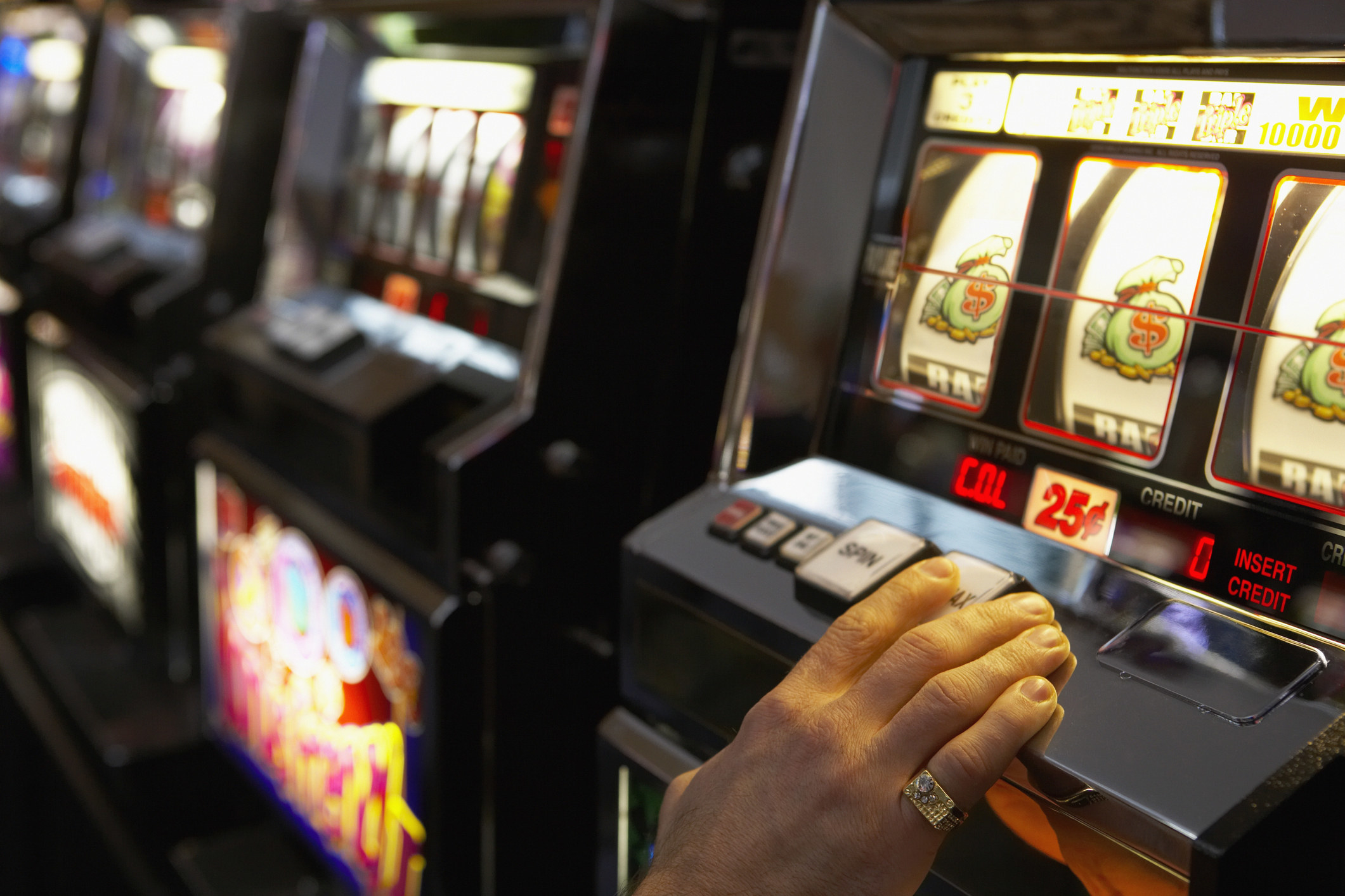 A hand presses a button on a slot machine
