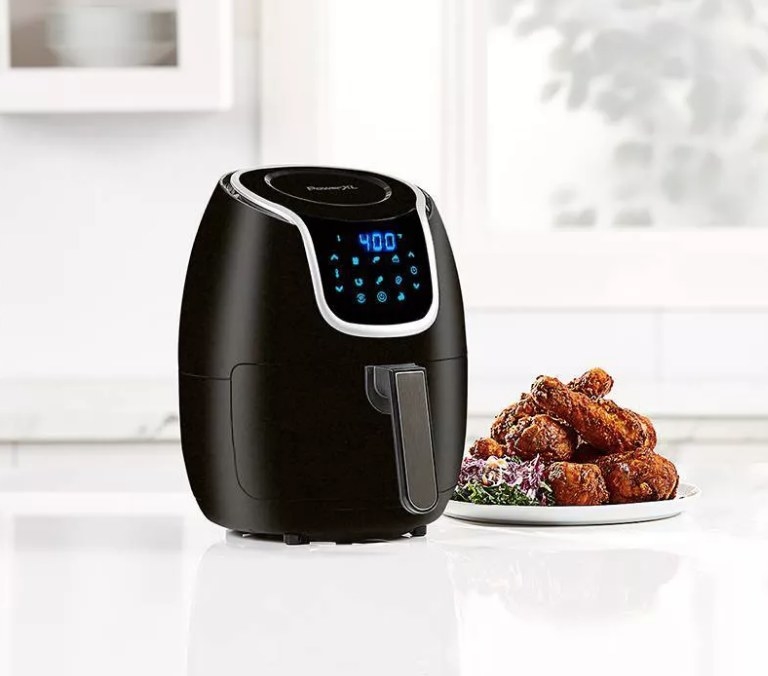 A black air fryer aside a plate of wings on a kitchen counter
