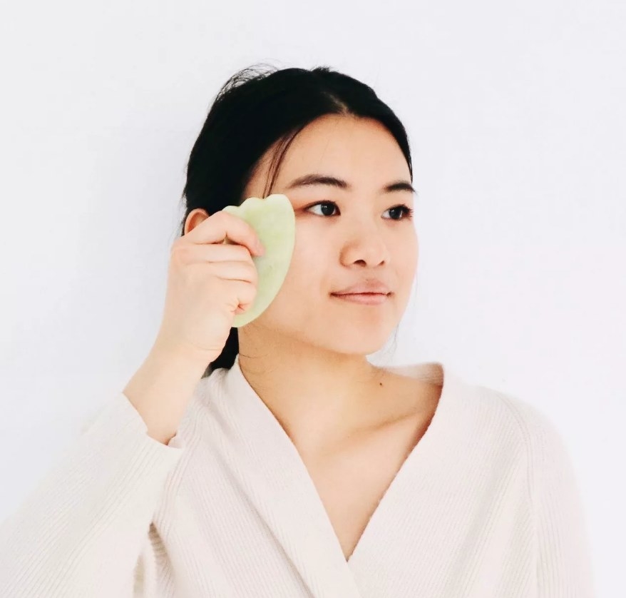 A model using a green Gua Sha facial massager tool