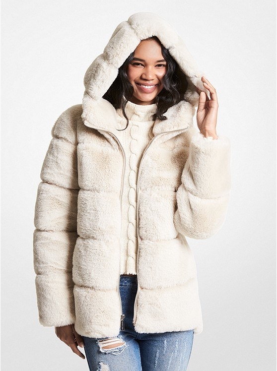 a smiling person wearing the oversized faux fur coat with a matching cableknit sweater and ripped jeans