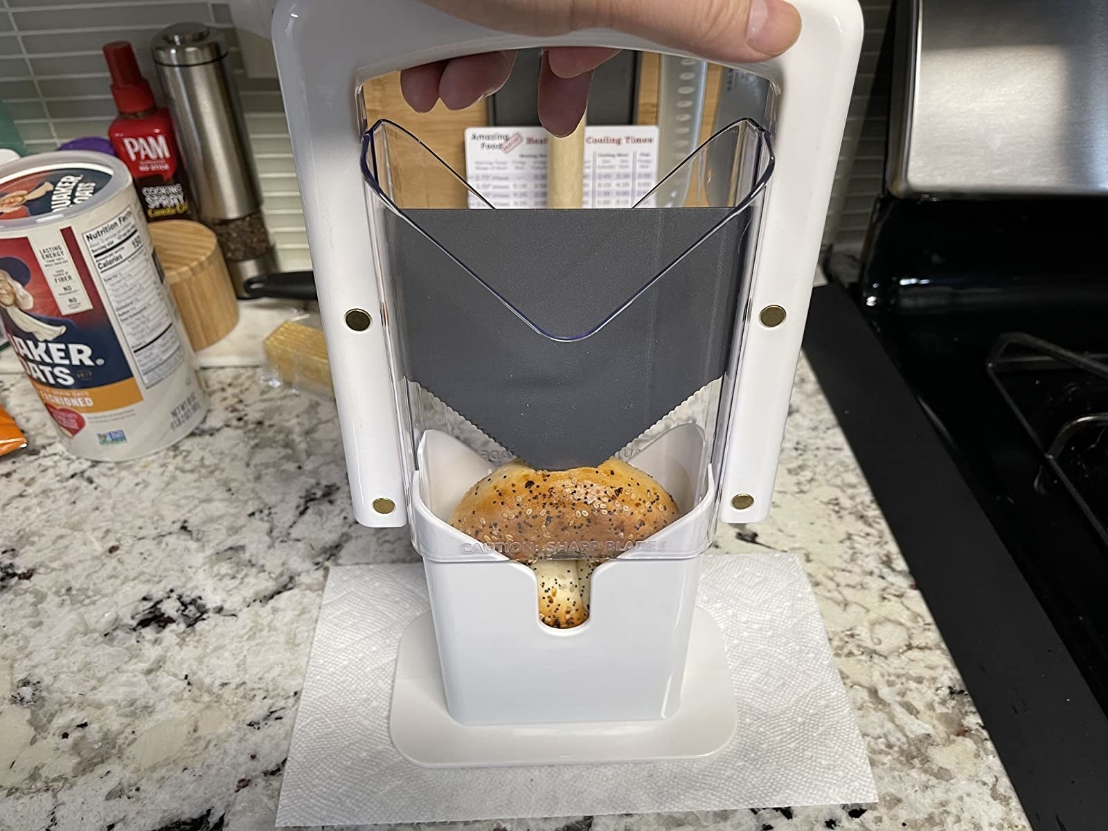 reviewer holding the bagel slicer in white with a bagel in the middle ready to be sliced