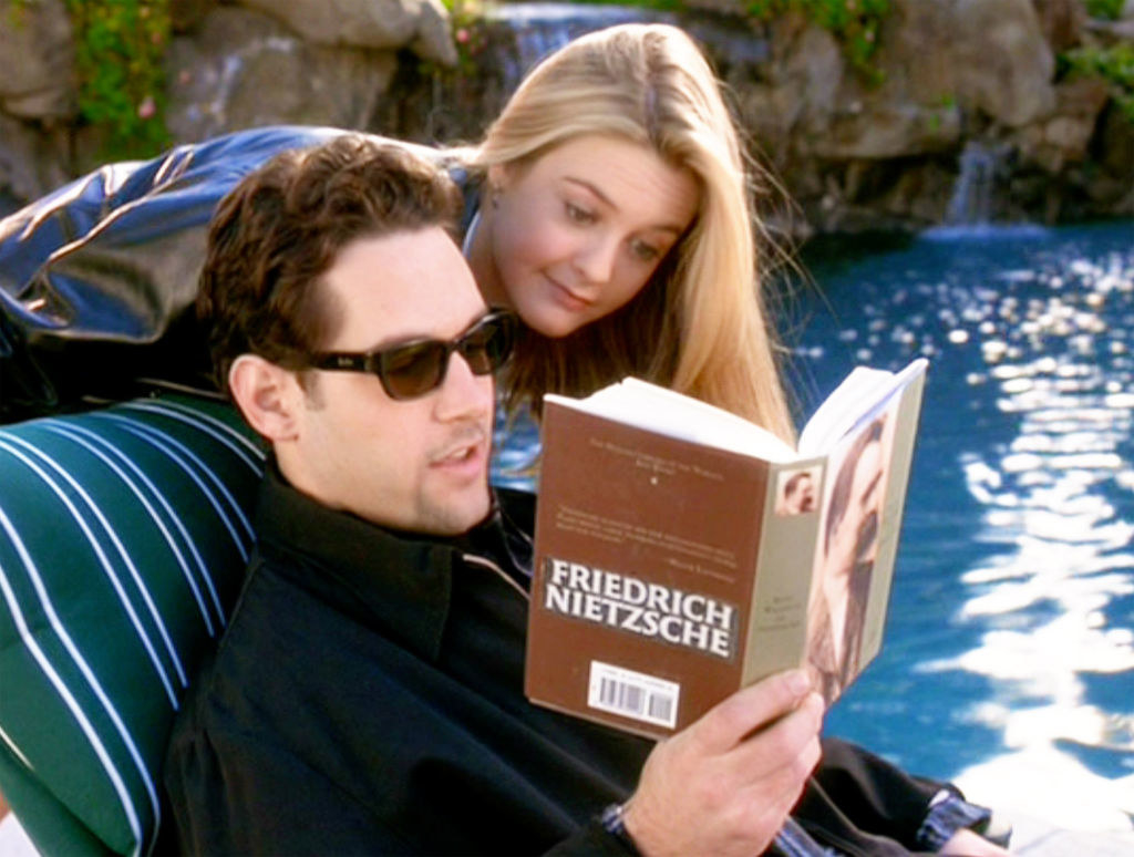Paul&#x27;s character reading a book about Friedrich Nietzsche next to a pool as Alicia&#x27;s character looks over his shoulder