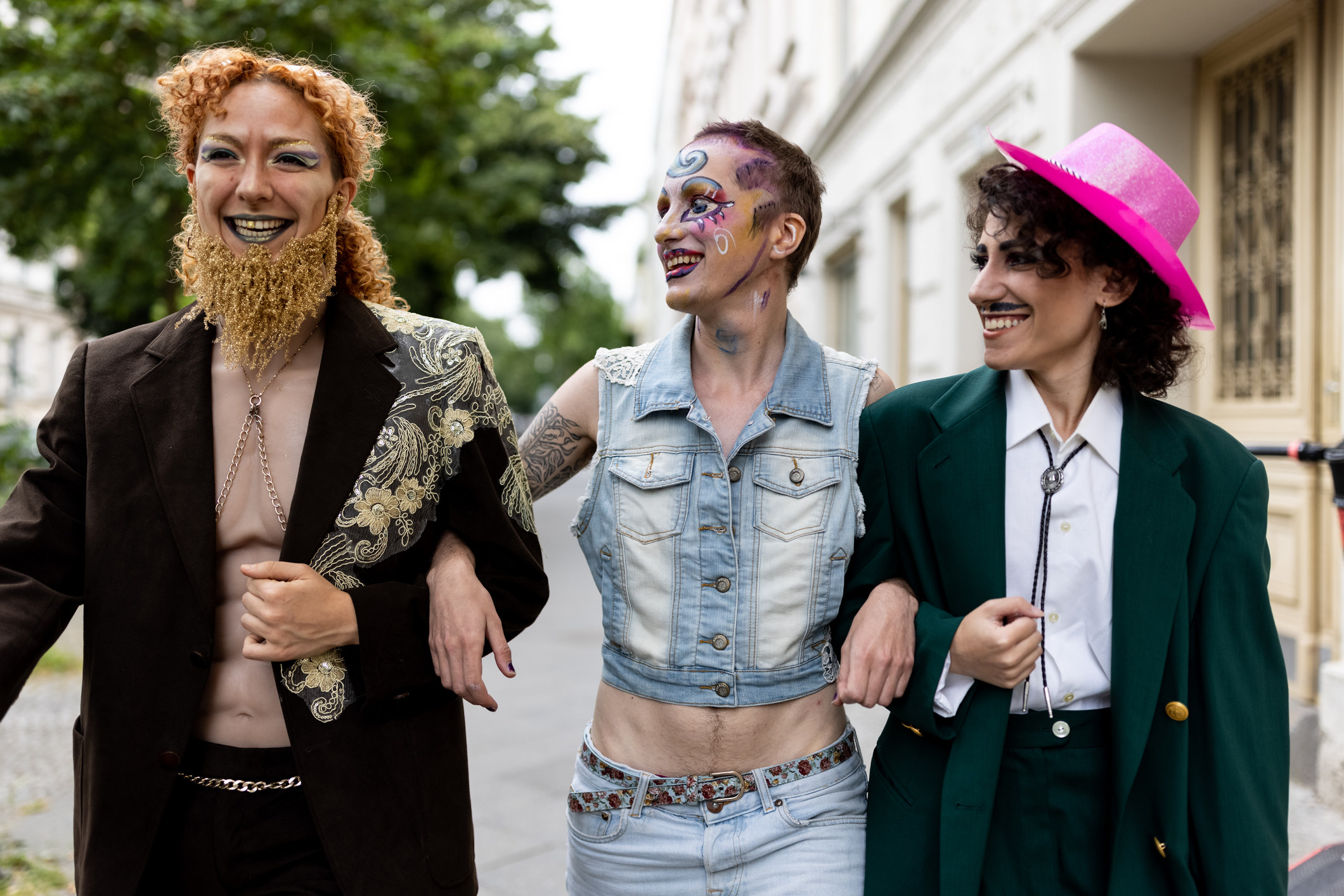 Group of three genderqueer friends walking outdoors in drag attire holding hands