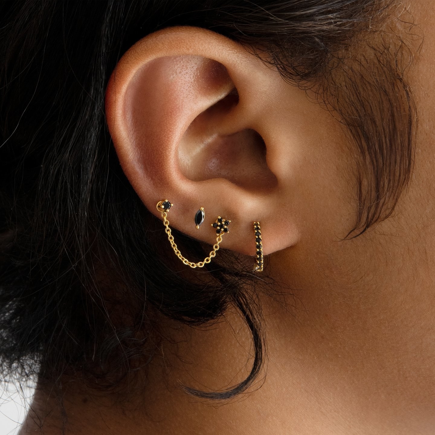 a model wearing four black stud earrings in various designs