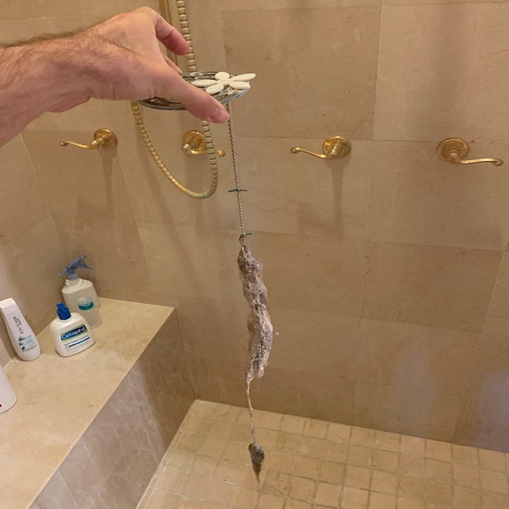 reviewer using the drain protector to pull hair out of a shower