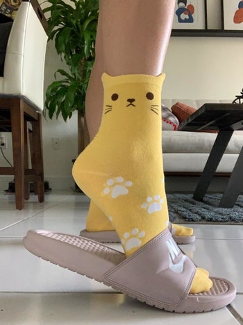 Reviewer wearing the yellow cat socks with slip-on sandals
