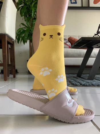 Reviewer wearing the yellow cat socks with slip-on sandals