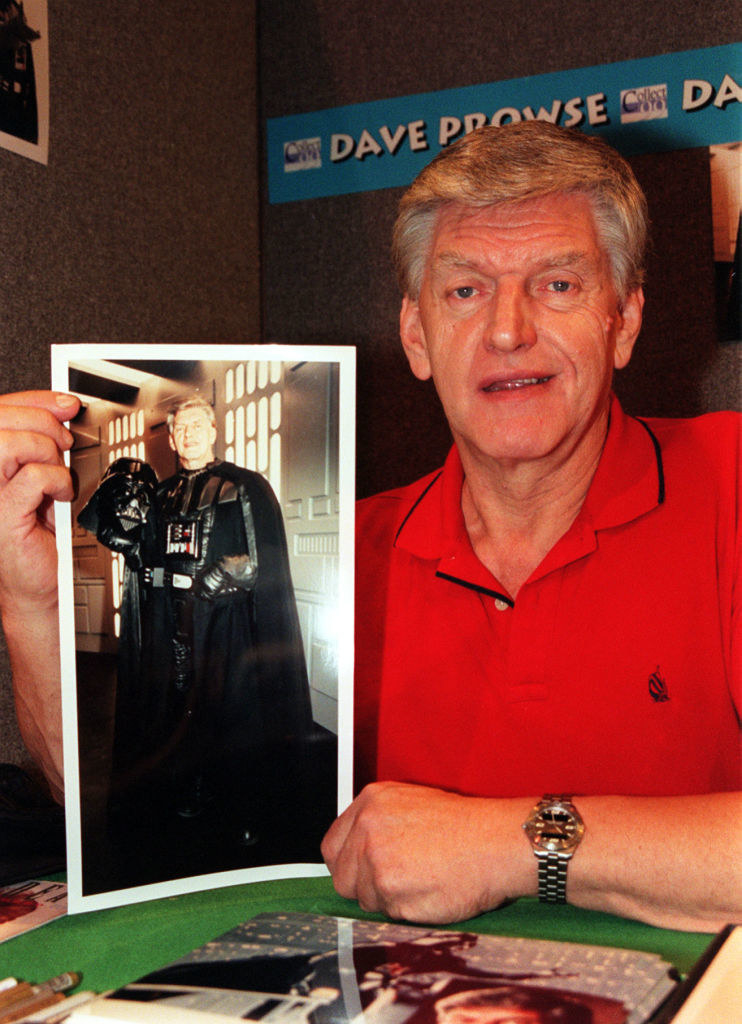 Prowse holding up a photo of him in costume