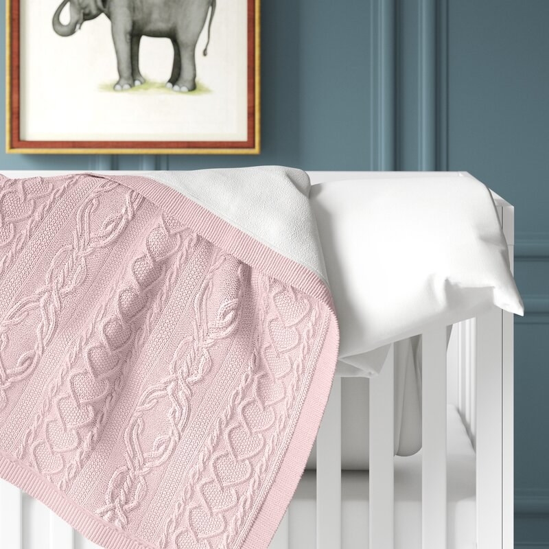 the pink cable knit blanket on a crib