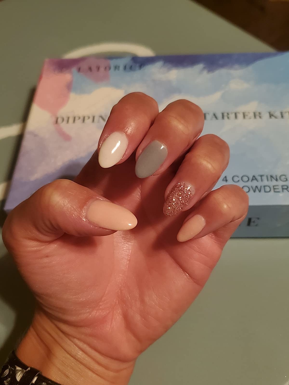 reviewer with pale pink thumb and pinky nails, a white index finger nail, a gray middle finger nail, and a pink glitter accent nail