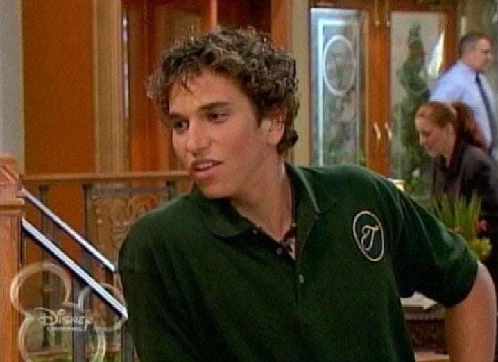 Aaron in a Tipton Hotel uniform with short curly hair on "Suite Life"