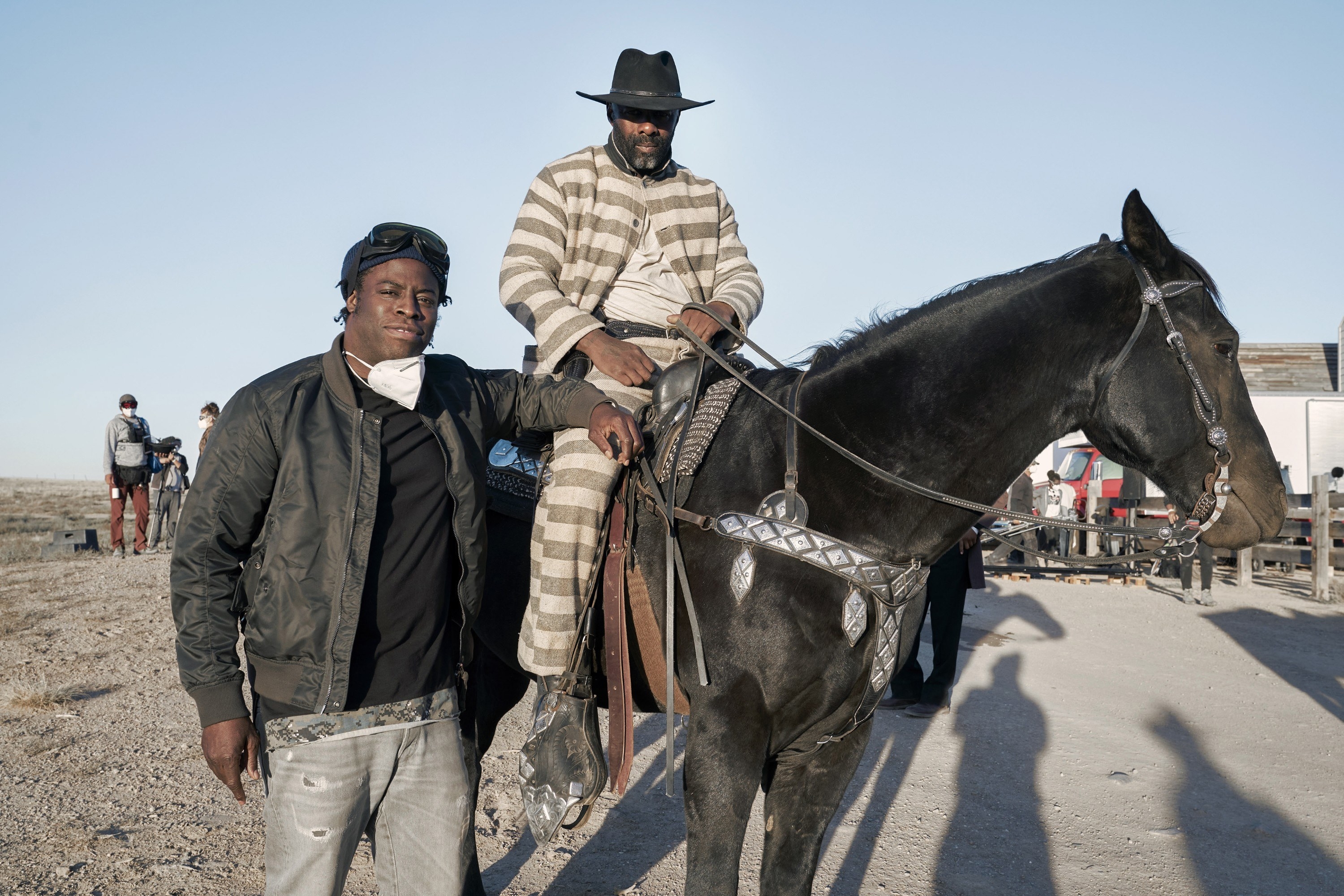 Director Jeymes Samuel stands next to Idris Elba who shits on a horse on set