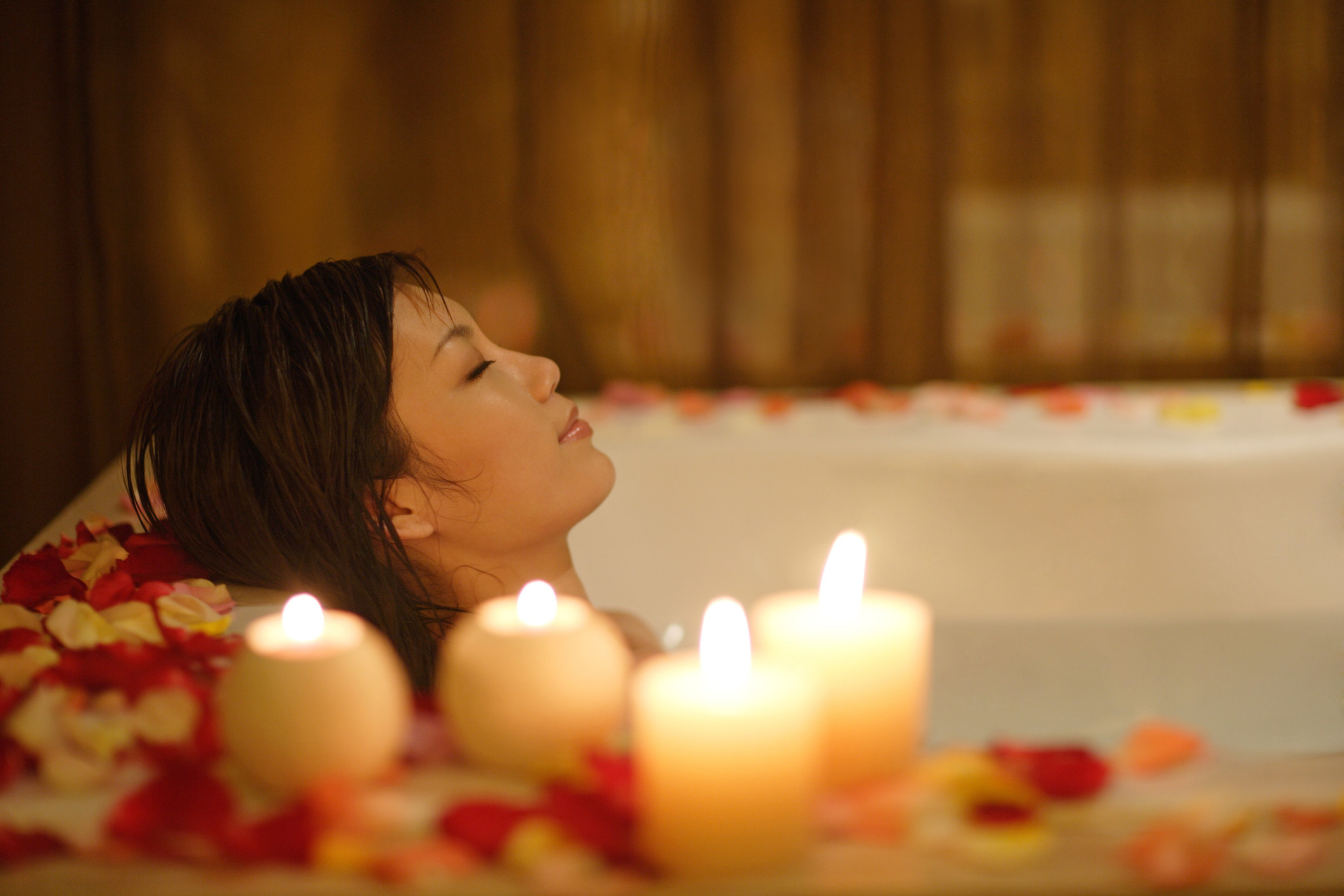 A woman in a bathtub with candles and rose petals
