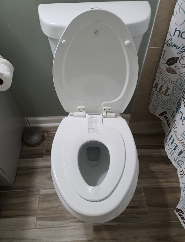 reviewer&#x27;s toilet seat with a smaller version hooked on top. it can easily be lifted up for adult use.