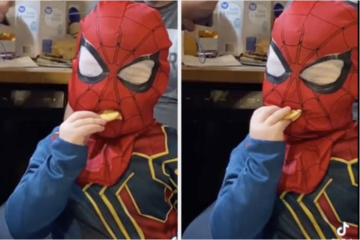 A kid in a spider-man mask tries to eat a cracker through the mask
