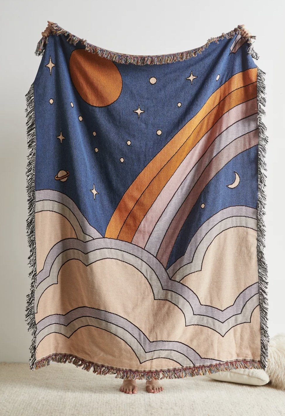 a throw blanket with fringes and drawings of the the night sky, a rainbow, and clouds